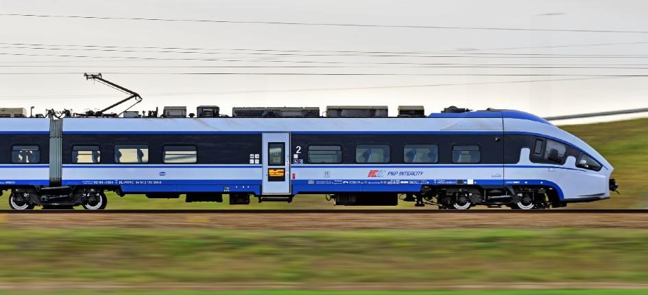 blue train crossing  from left to right over green field.