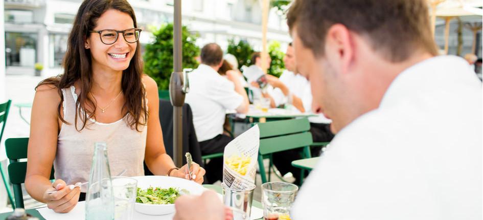 Ein junger Mann und eine junge Frau essen draussen in einem Restaurant zu Mittag. 