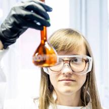 woman looking at test tube with orange liquid in it
