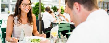 Ein junger Mann und eine junge Frau essen draussen in einem Restaurant zu Mittag. 