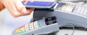 A hand holds a smartphone over a payment terminal.